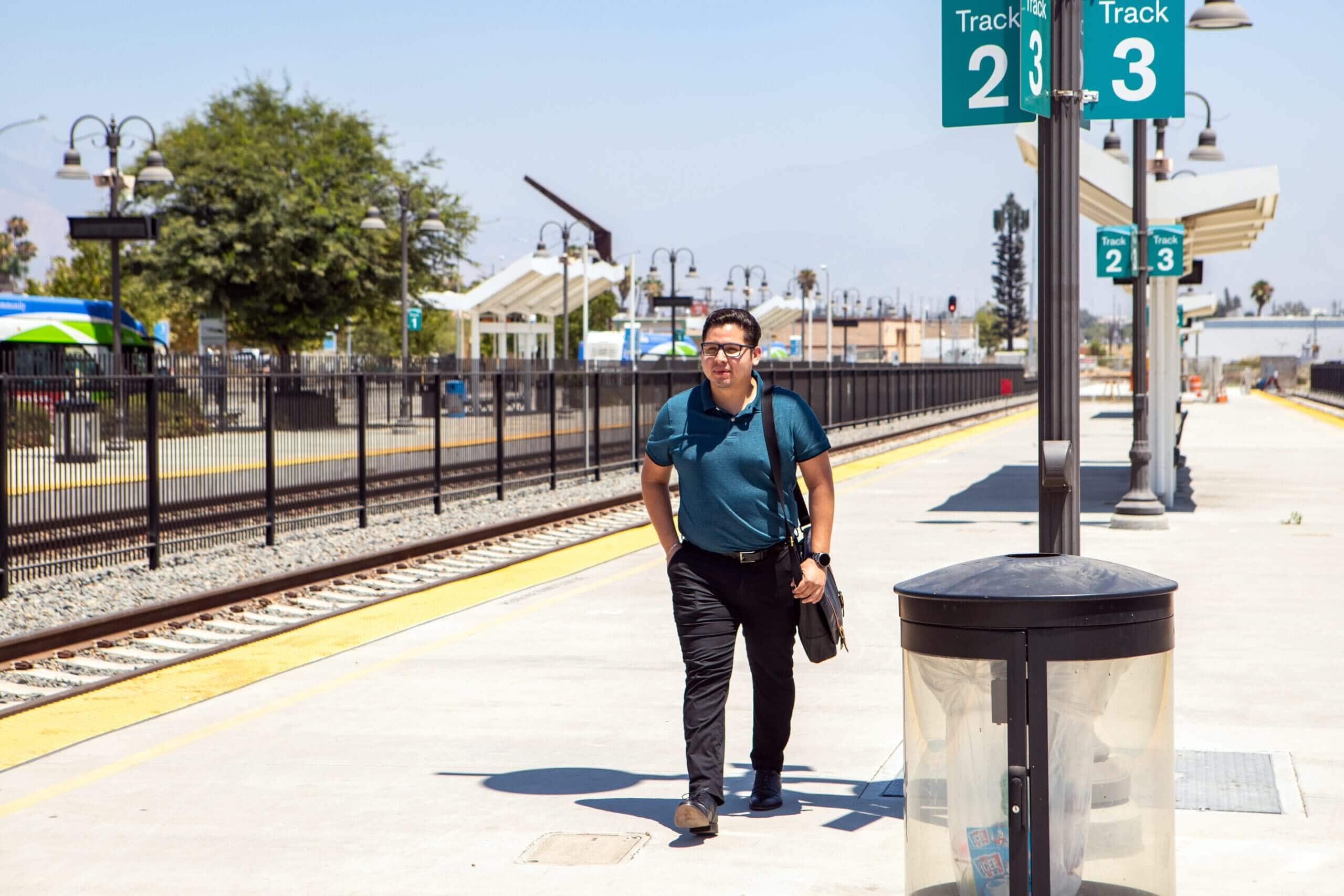 Image of man with messenger bag walking next to train tracks